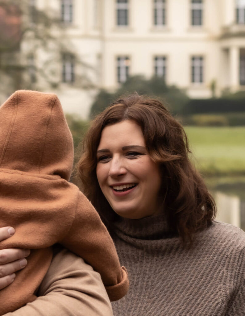 Familienfotografin Dülmen & Umgebung, Familienshooting Outdoor, Baby auf dem Arm vom Papa und schaut nach hinten zur Mama.