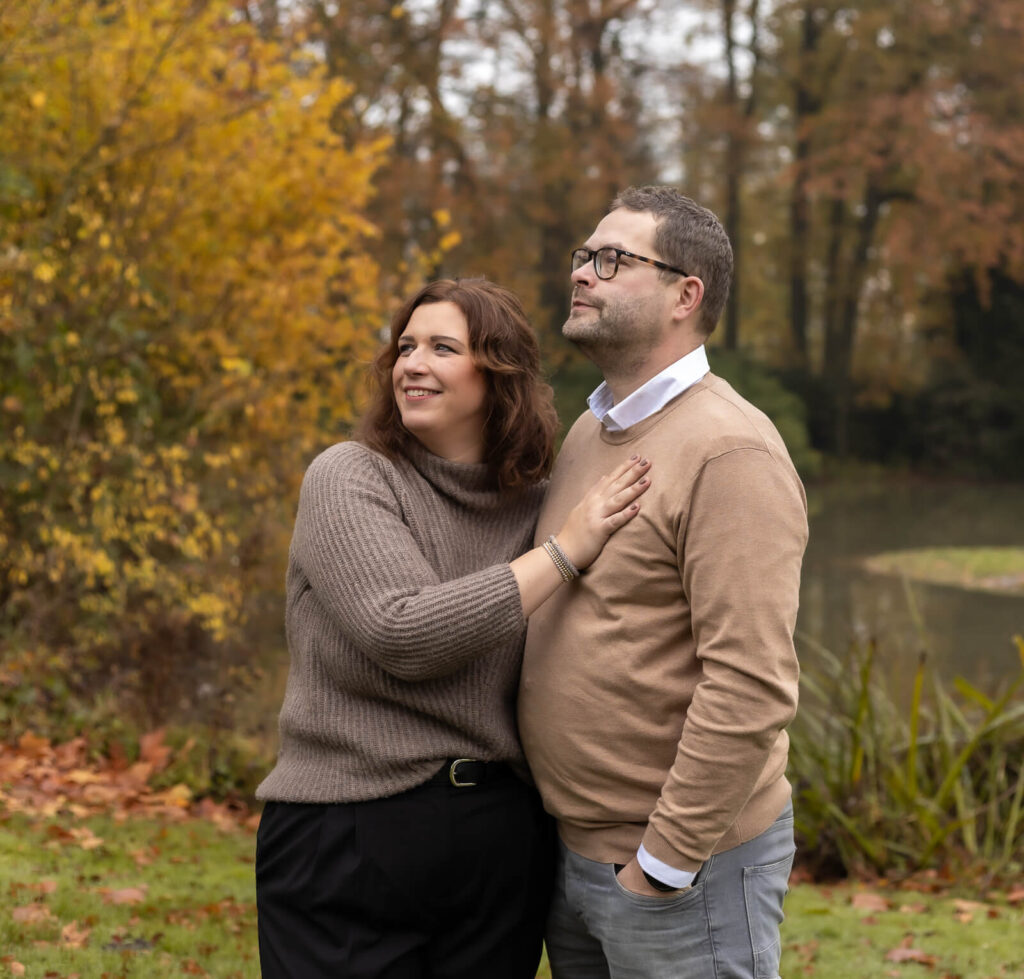 Familienfotografin Dülmen & Umgebung, Familienshooting Outdoor, der Mann hält seine Frau seitlich im Arm und die Hand der Frau ruht auf seiner Brust, während beide seitlich lächelnd in Richtung Himmel schauen.