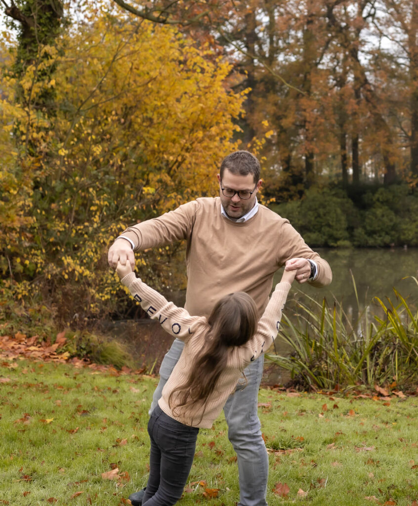 Familienfotografin Dülmen & Umgebung, Familienshooting Outdoor, ein Papa tanzt mit seiner Tochter in dem er ihre Arme hoch hält und sie dreht, dabei tanzt die Tochter mit dem Rücken zur Kamera.