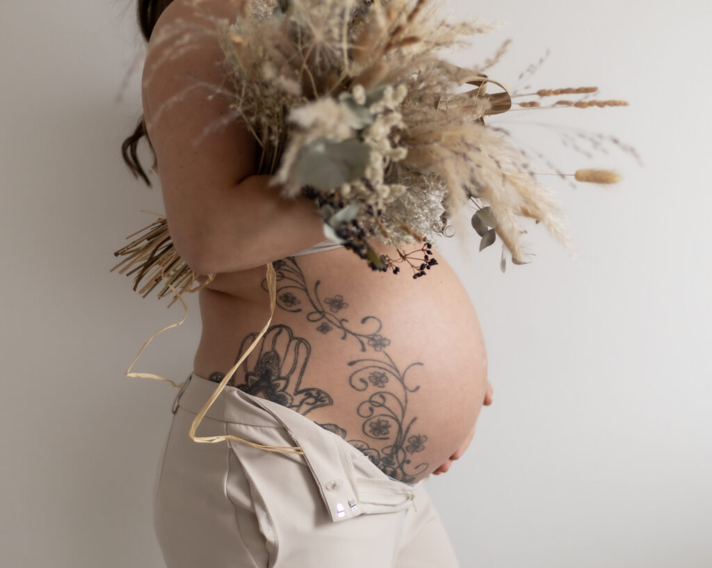 Freier Babybauch seitlich mit Strauß Trockenblumen
