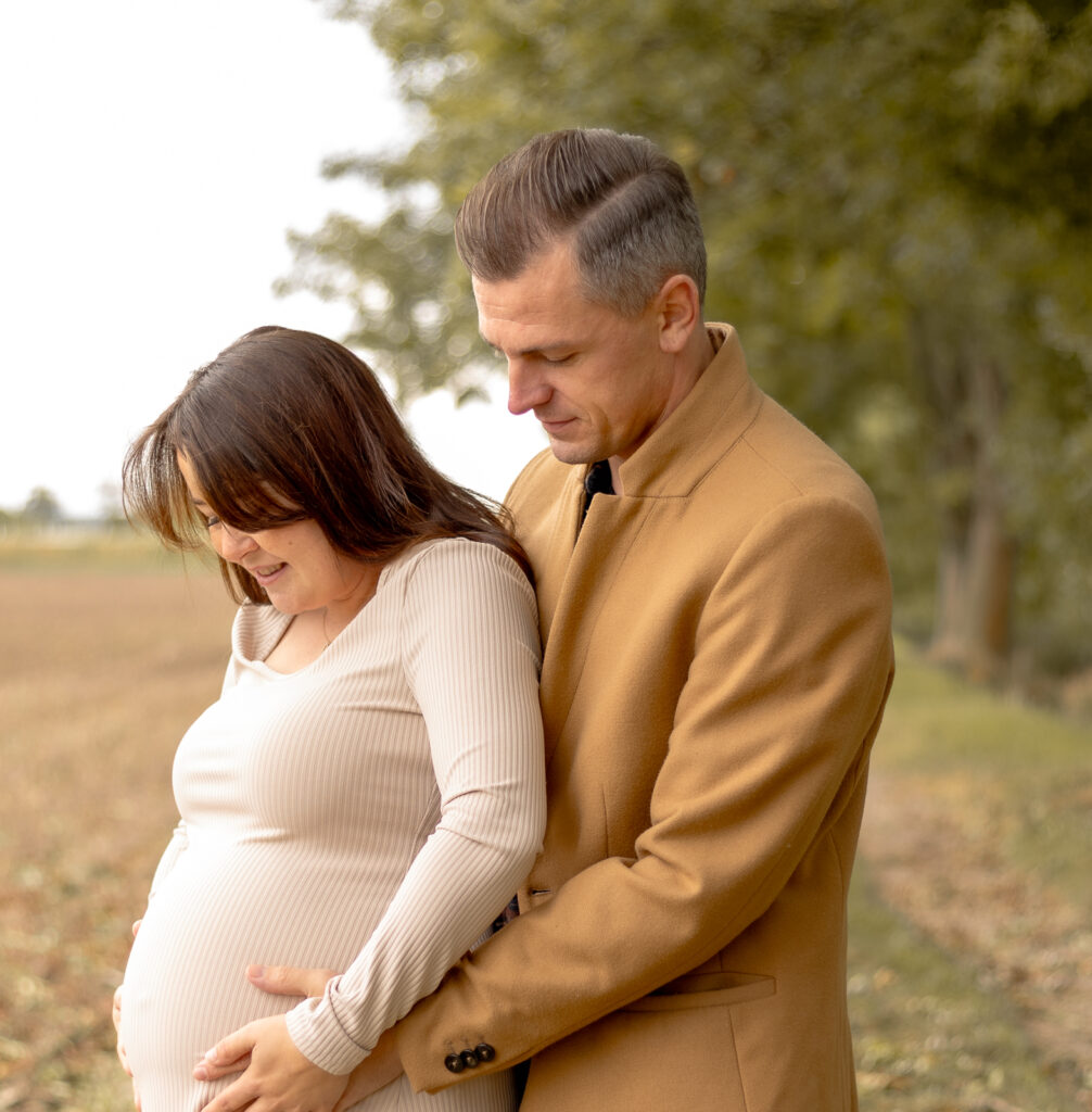 Mann legt seine Hände von hinten auf den Babybauch seiner Frau