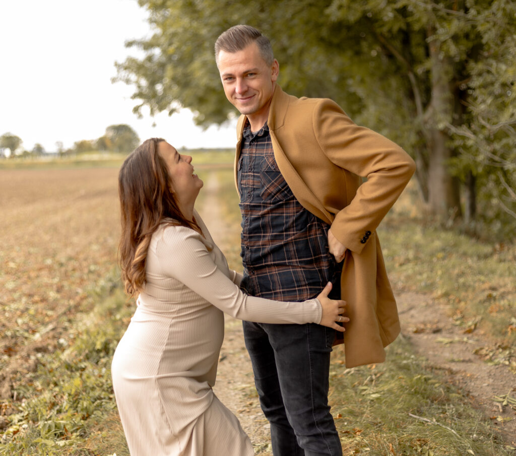 Schwangere Frau kommt lachend aus der Pose, wo sie ihren Mann auf den Bauch küsst