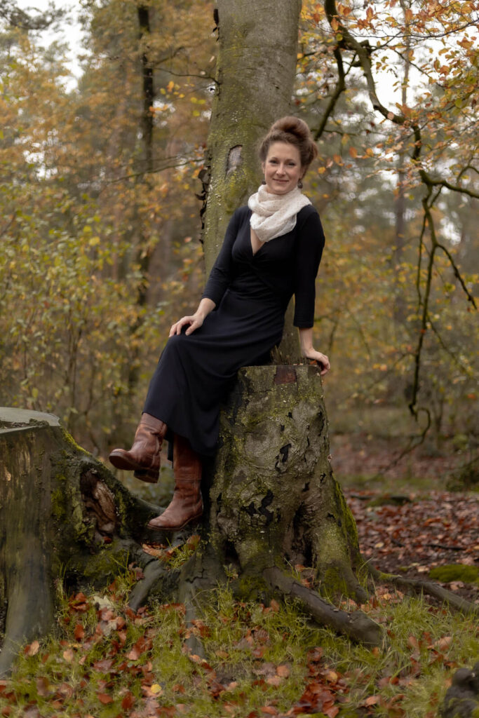 Mama sitzt auf einem Baumstamm & lächelt in die Kamera