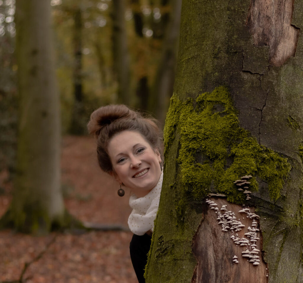 Mama schaut lachend hinter einem Baum hervor