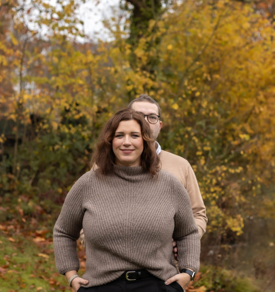 Mann steht hinter seiner Frau & beide schauen zur Kamera