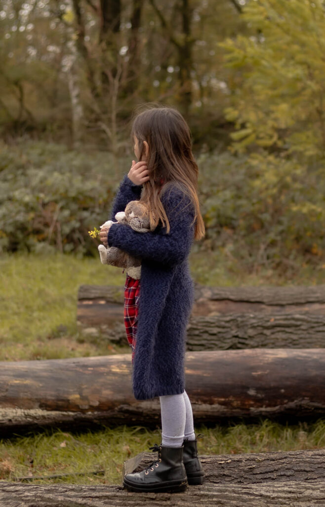 Tochter steht seitlich an einem Baumstamm & schaut nach hinten