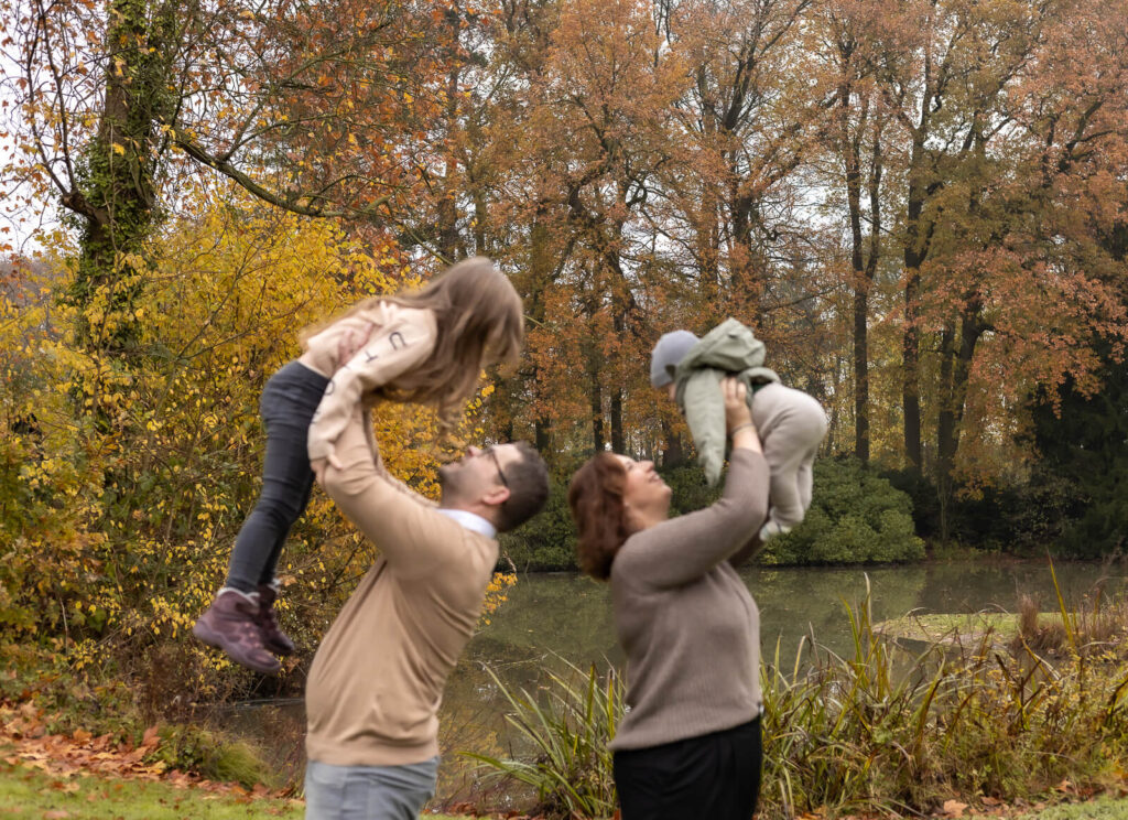 Mama & Papa stehen mit Rücken aneinander & halten ihre 2 Kinder hoch