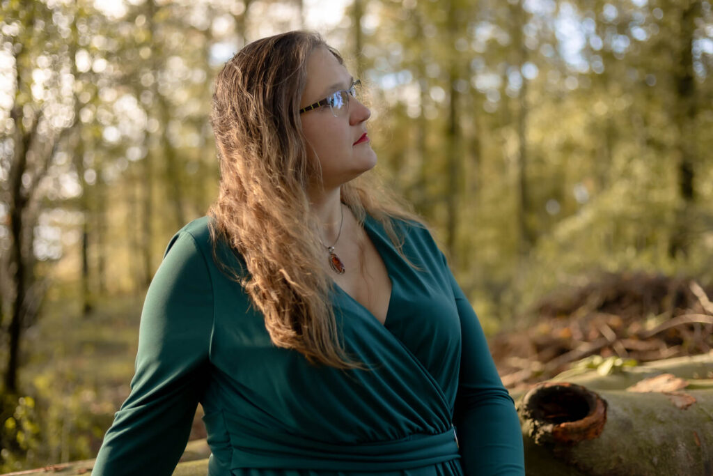 Frau sitzt auf Baumstamm & schaut von der Kamera weg