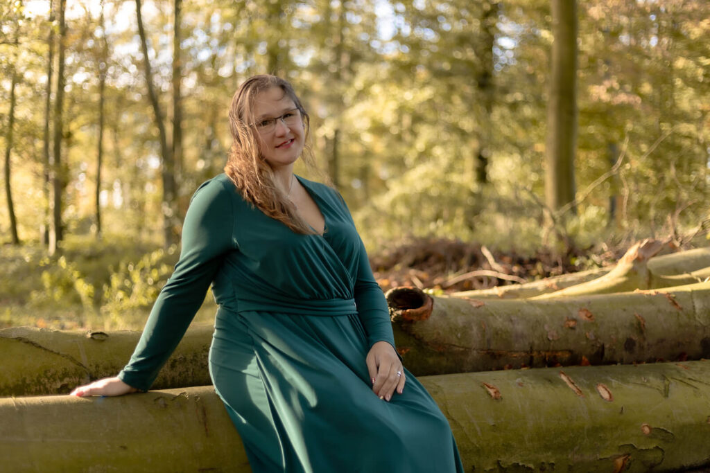 Frau sitzt auf einem Baumstamm & schaut lächelnd in die Kamera