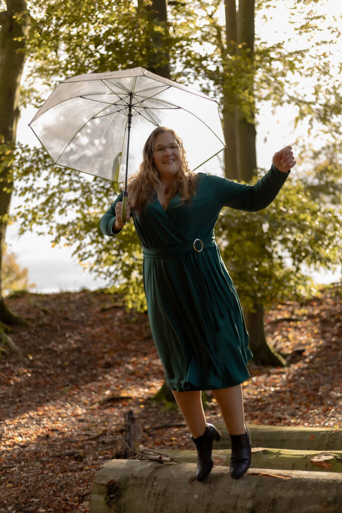 Frau springt vom Baumstamm mit Regenschirm über den Kopf