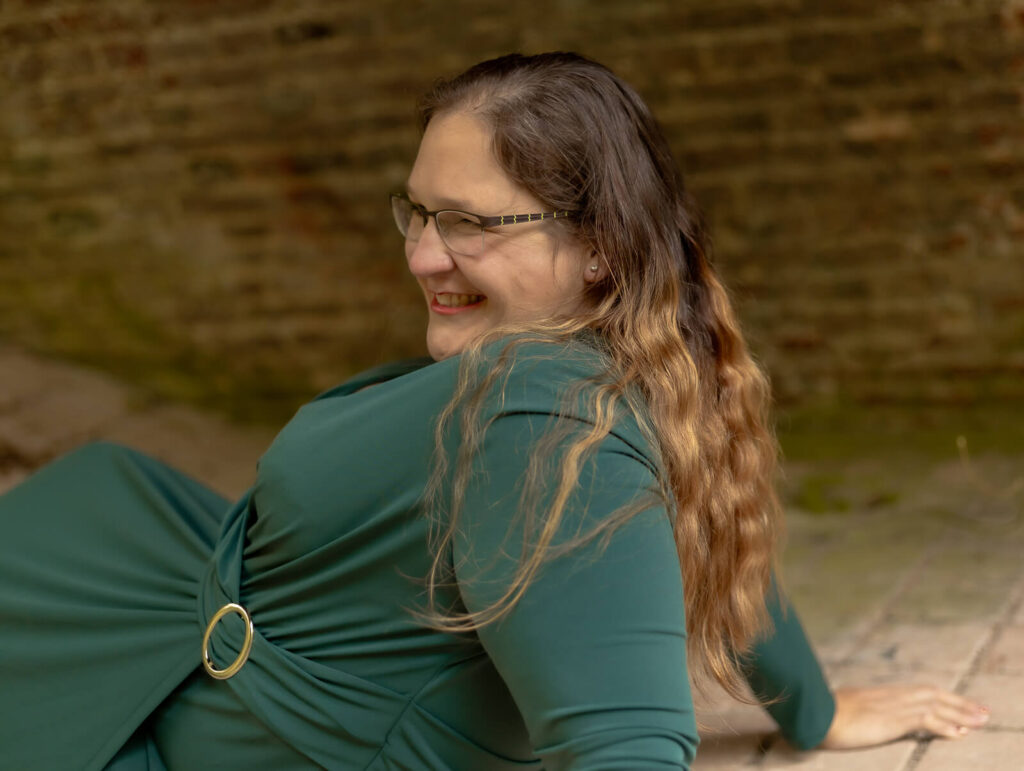 Frau liegt lachend unter einer Brücke auf einer Erhöhung auf ihre Arme gestützt