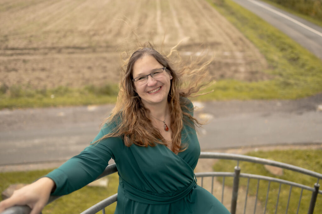 Frau steht an einem Gelände & schaut zur Kamera