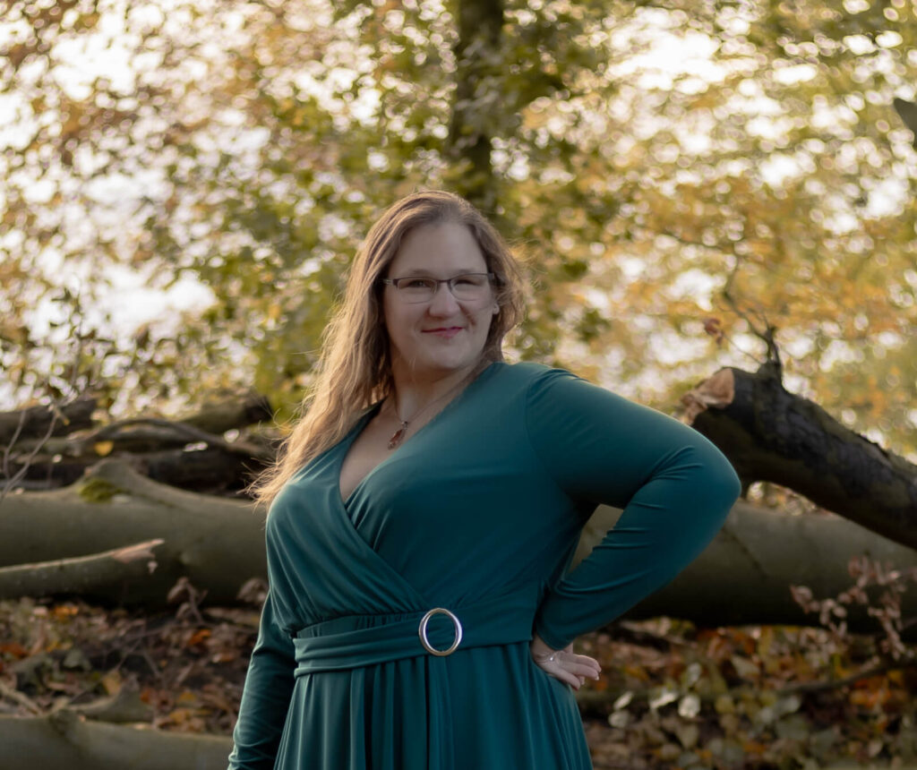 Frau steht mit Hand in der Hüfte gestützt & schaut in die Kamera