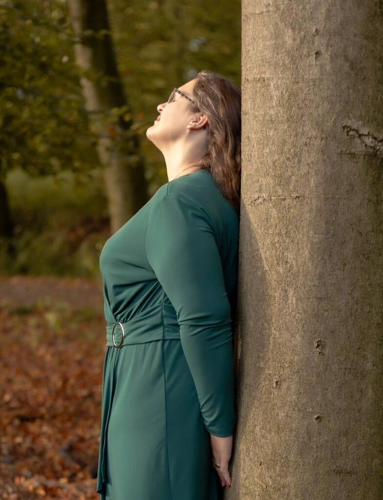 Frau ist mit dem Rücken & geschlossenen Augen an einem Baum gelehnt