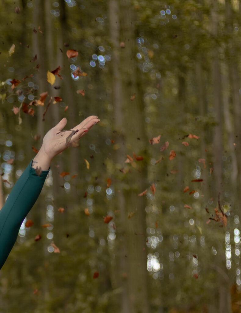 Detailaufnahme einer weiblichen Hand, die Blätter in die Luft wirft